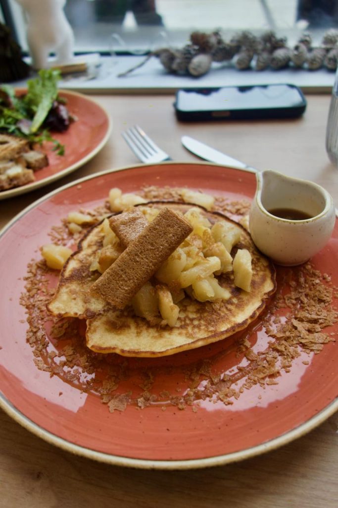 Pancake, pommes rôties et crêpes dentelles dans une assiette en grès rouge accompagnés d'un pot de caramel