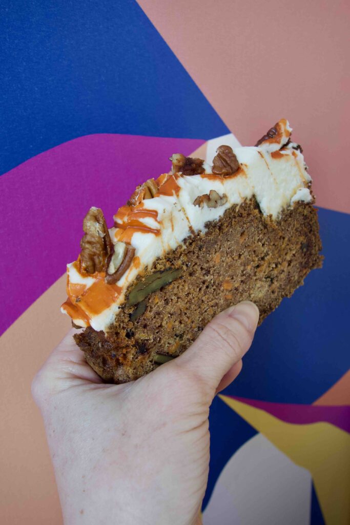 Une part de carrot cake au glaçage épais surmonté de noix de pécan