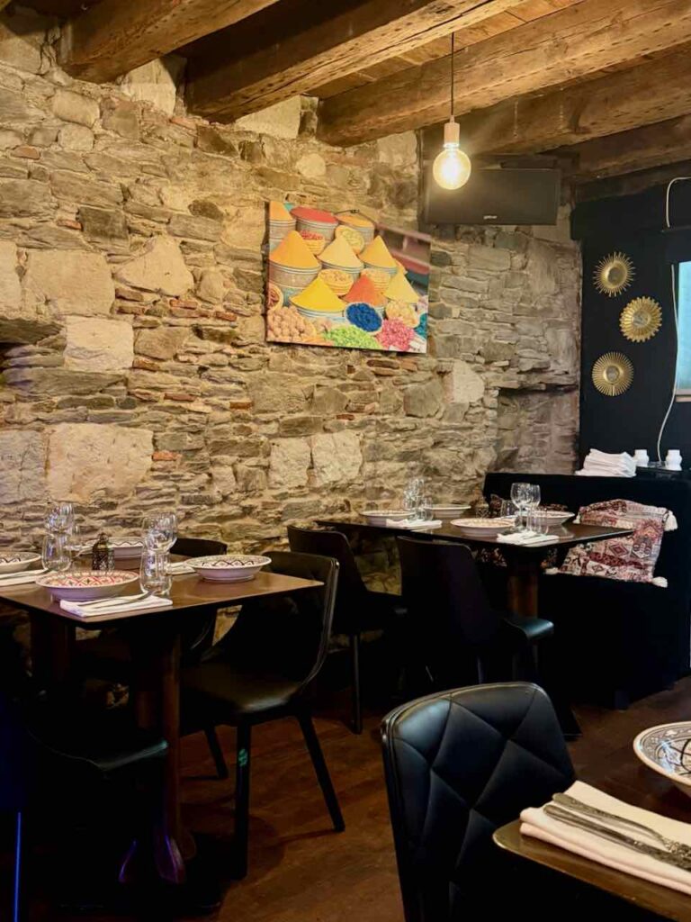 Chaises et tables noires à l'intérieur du restaurant, mur en pierres.