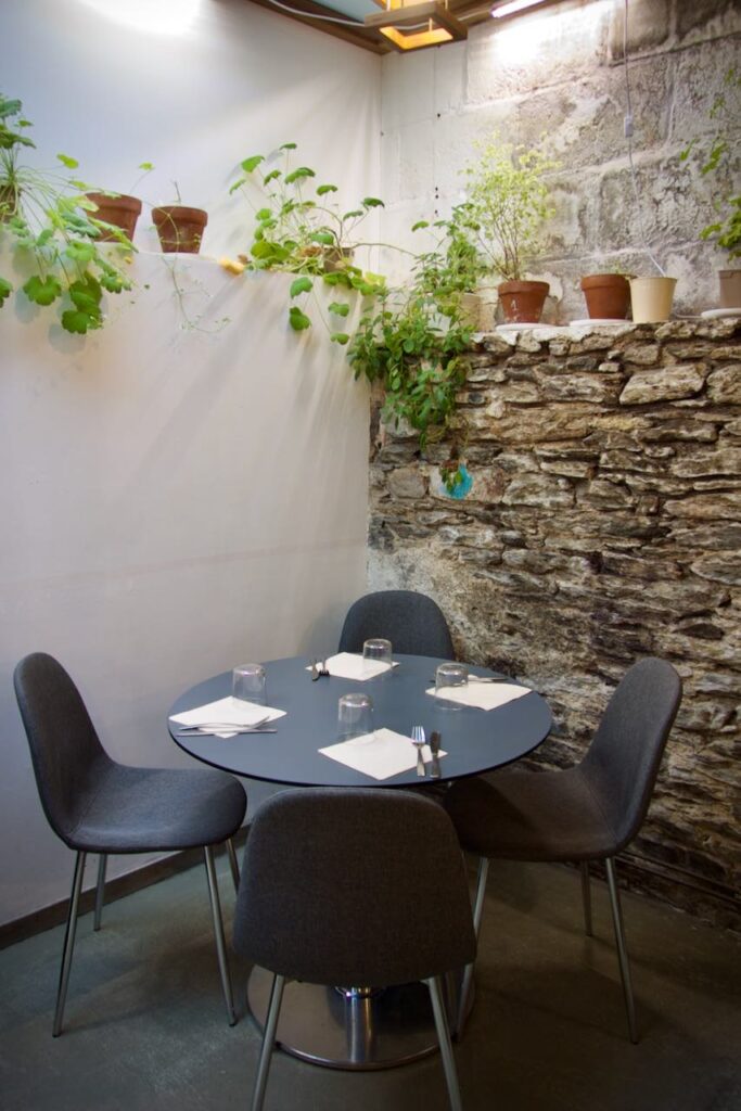 Table ronde et chaise noire devant un mur de pierres de taille sur lequel sont posés des pots d'herbes aromatiques