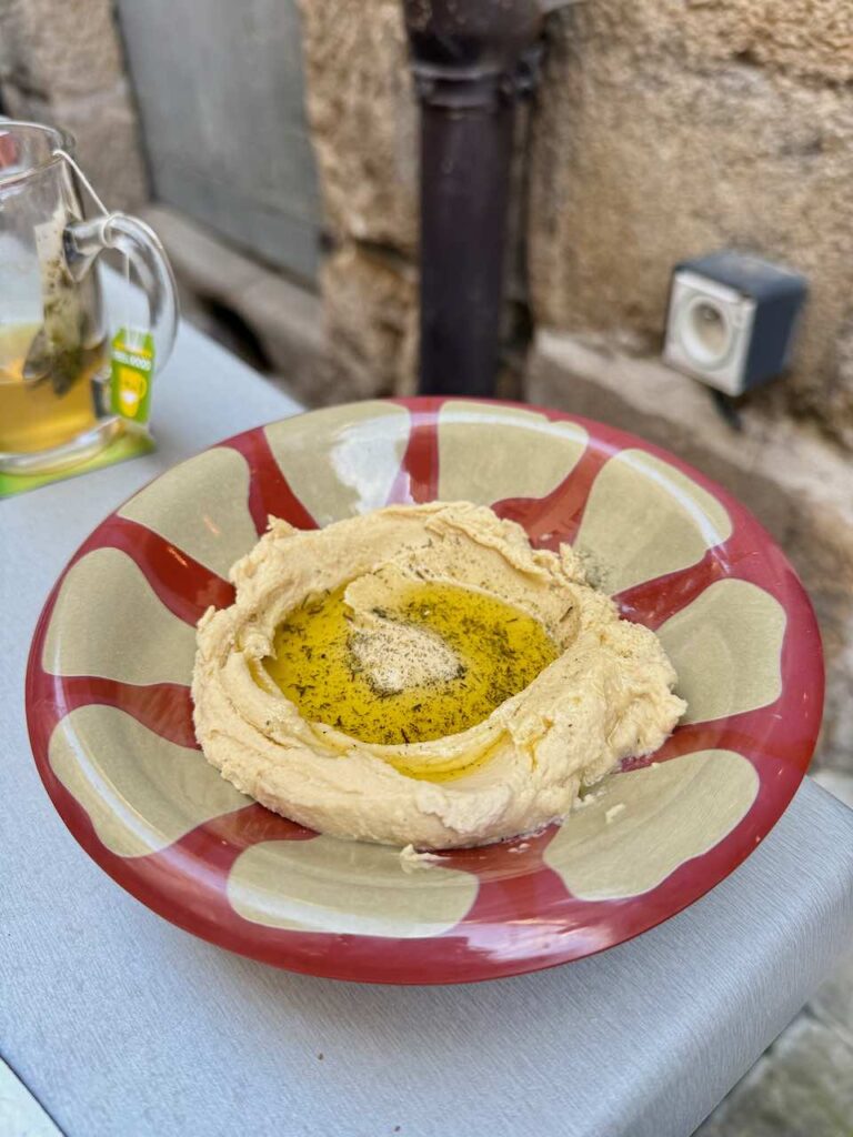Hoummous dans une assiette creuse rouge et beige, surmonté d'huile d'olive