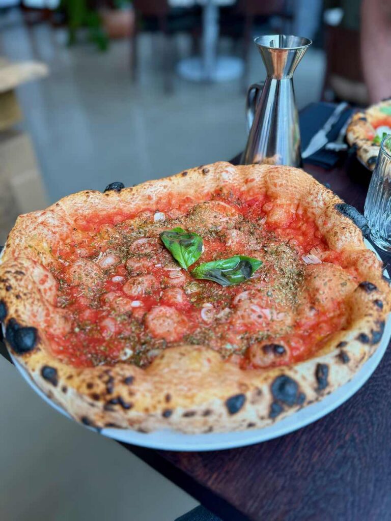 Pizza Marinara dans une grande assiette blanche, un contenant de sauce piquante en métal au second plan