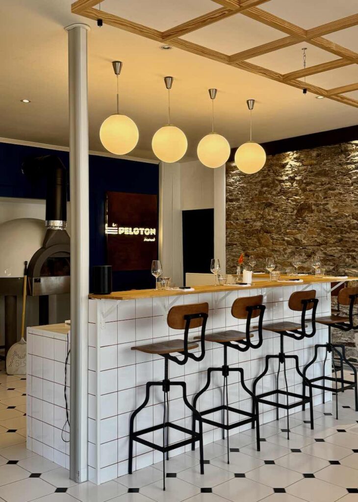 Comptoir carrelé blanc avec chaises hautes acier et bois, four à pizza au second plan