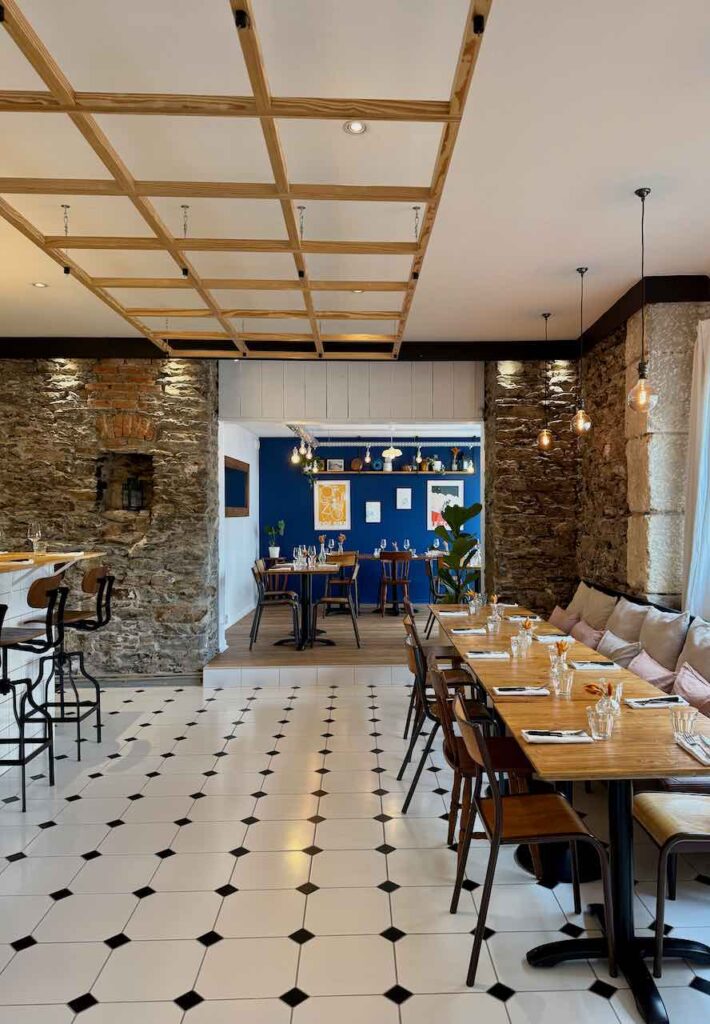 Intérieur du restaurant avec un sol carrelé blanc et noir, une grande tablée à droite et une petite salle aux murs bleus dans le fond