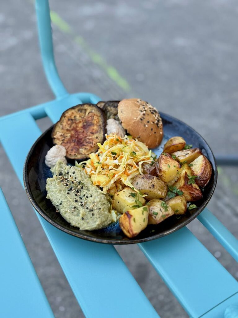 Assiette d'aubergines, houmous, pommes de terre et coleslaw posée sur une chaise de jardin bleue