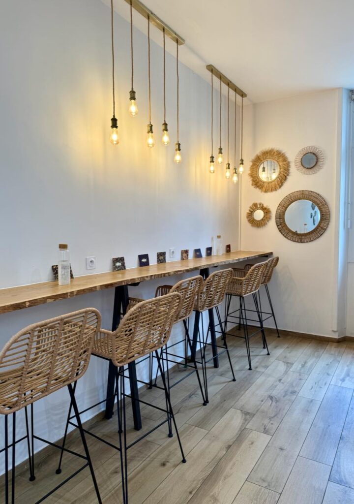 Chaises hautes rotin et fer forgé noir, table bar en bois, miroirs en paille au mur