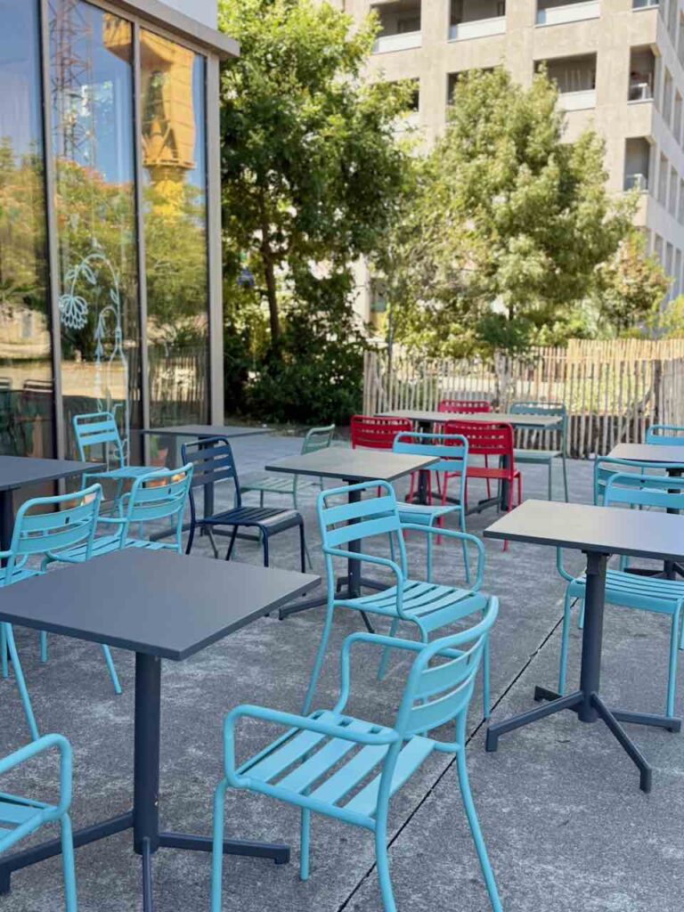 Terrasse du Labo Diva avec des tables noires, des chaises bleues et rouges