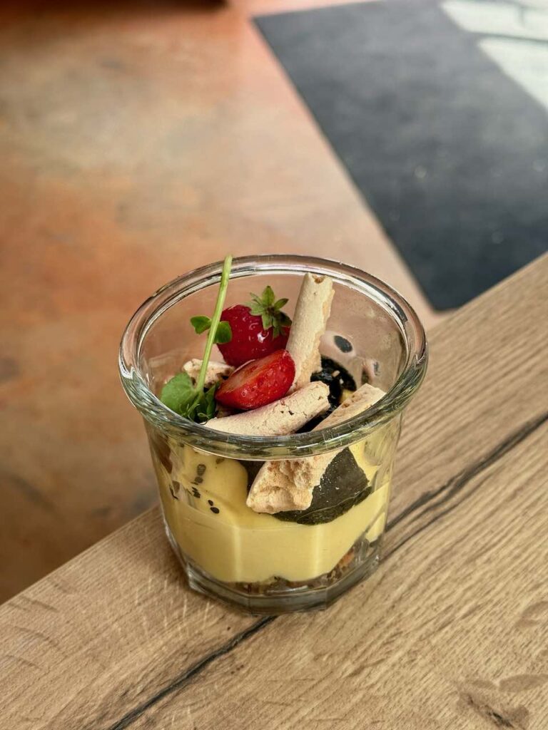 Crémeux citron, meringue, aromate et fraise dans une verrine sur une table en bois