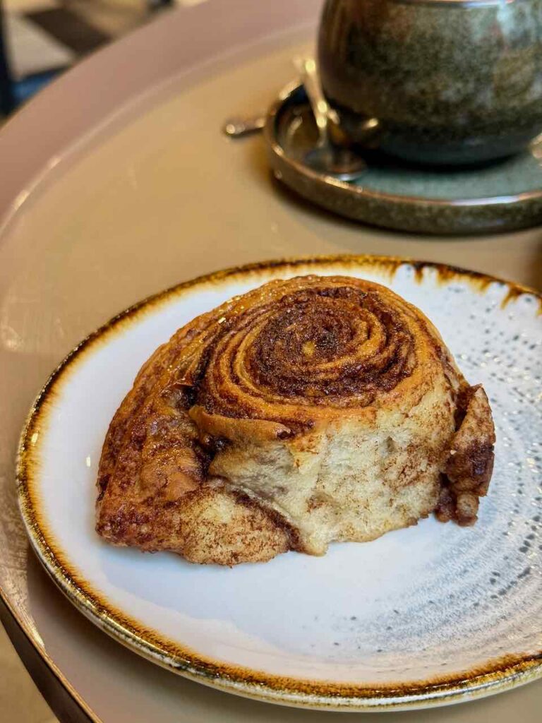 Cinnamon roll brioché dans une assiette en grès blanche à liseré marron/doré