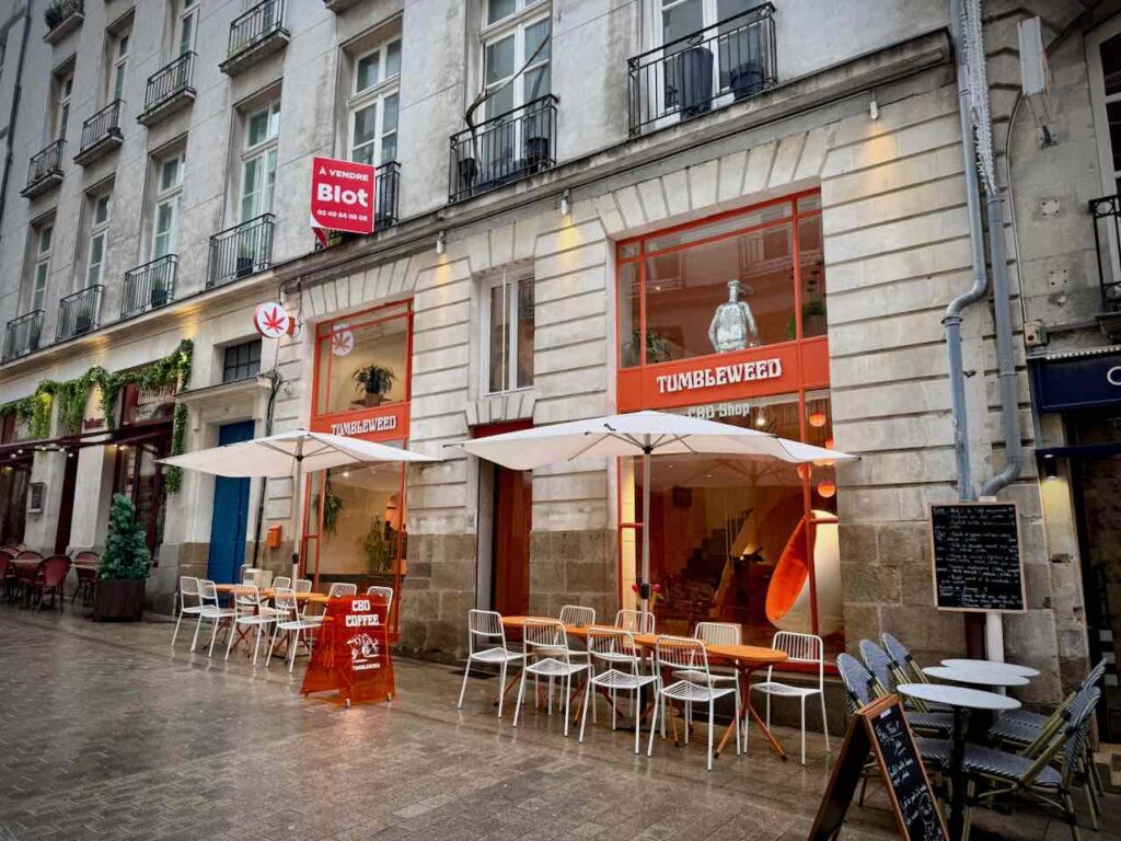 Devanture du coffee shop orange avec chaises et tables avec parasol en terrasse