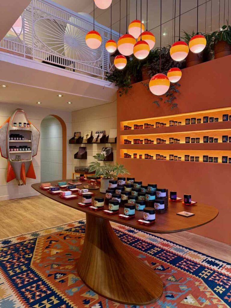 Magasin de CBD avec grande table centrale design en bois sur laquelle sont posés des produits CBD, grand tapis au sol, vinyles en arrière plan