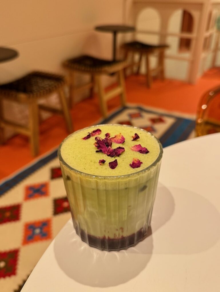 Matcha latte surmonté de pétales de roses avec de la framboise dans le fond du verre