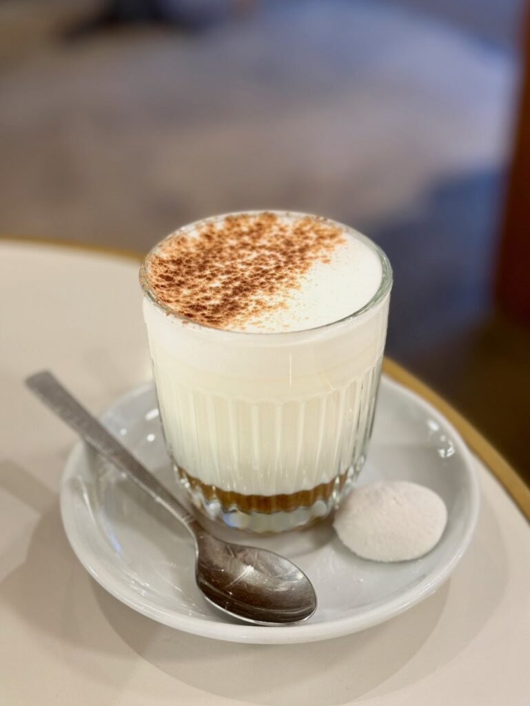 Pumpkin spice latte dans un verre transparent à stries, fine couche de sirop à la base, épices sur la mousse, le tout accompagné d'une guimauve