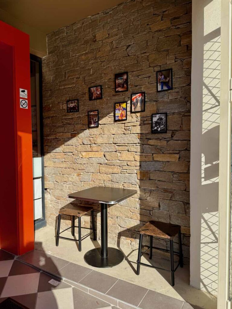 Entrée avec une table noire, deux tabouret, mur en pierre et photos accrochées