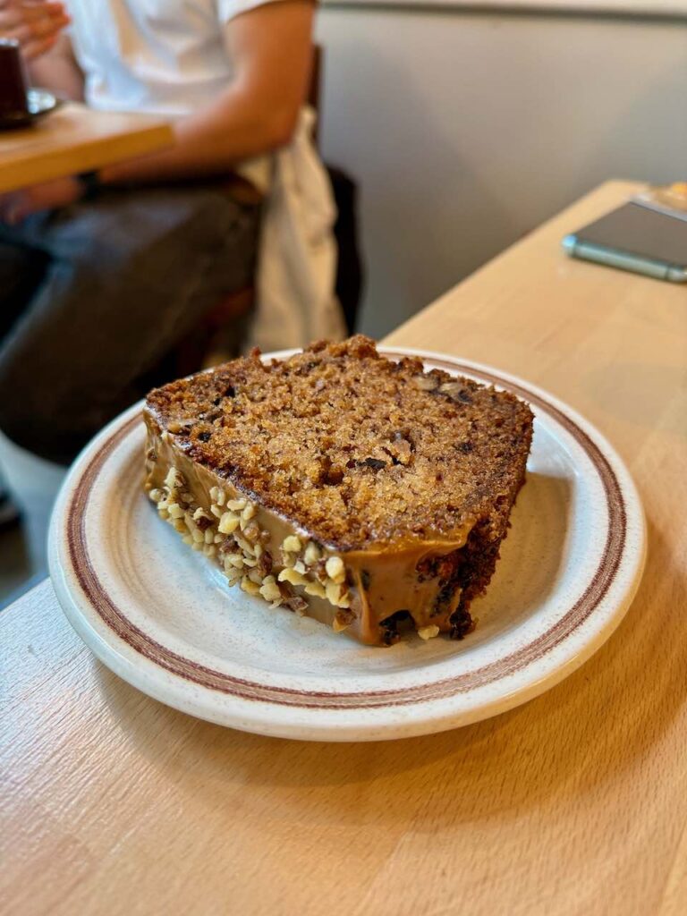 Banana bread vegan surmonté de chocolat noir et pralin dans une assiette blanche à liseré marron