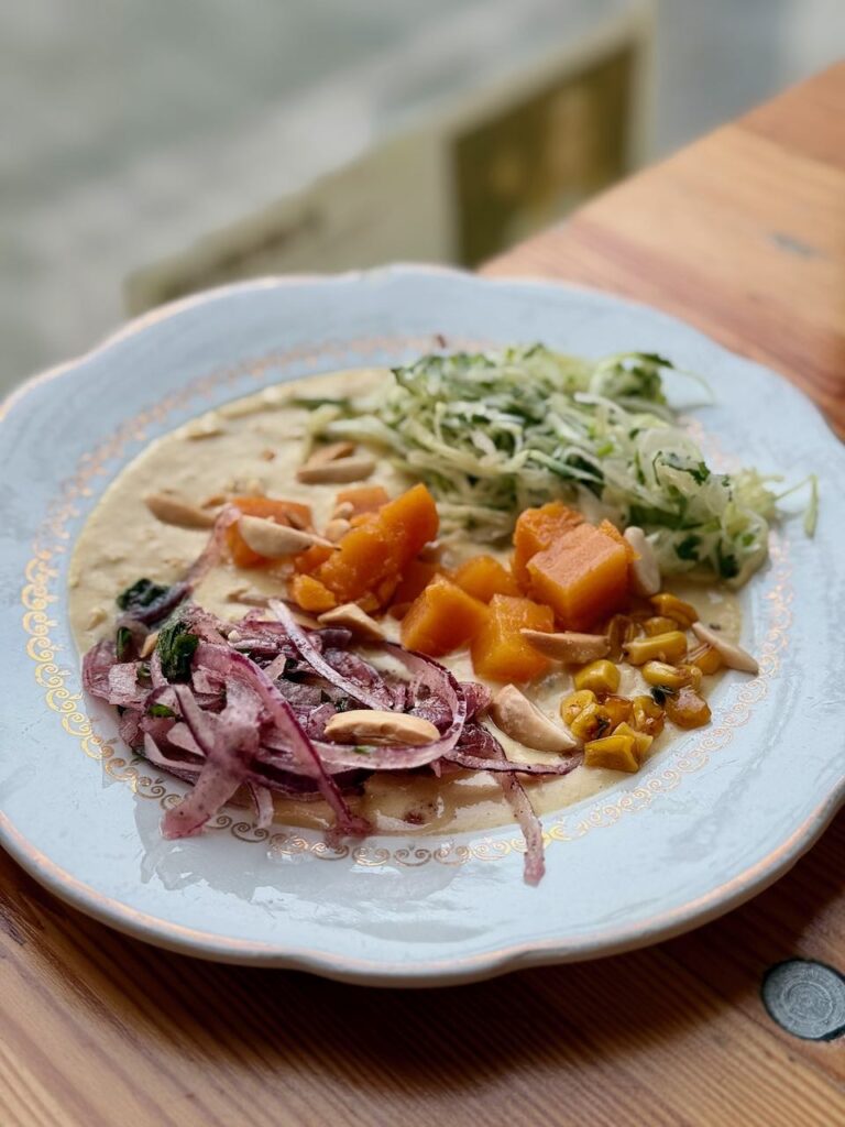 Assiette de chou, oignon rouge, patate douce et maïs sur une crème, le tout dans une assiette vintage blanche à liseré doré