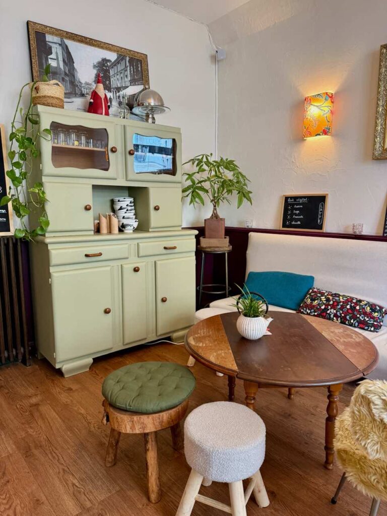 Vieux buffet restauré vert anis à l'arrière plan, table basse ronde en bois, tabourets moelleux au premier plan