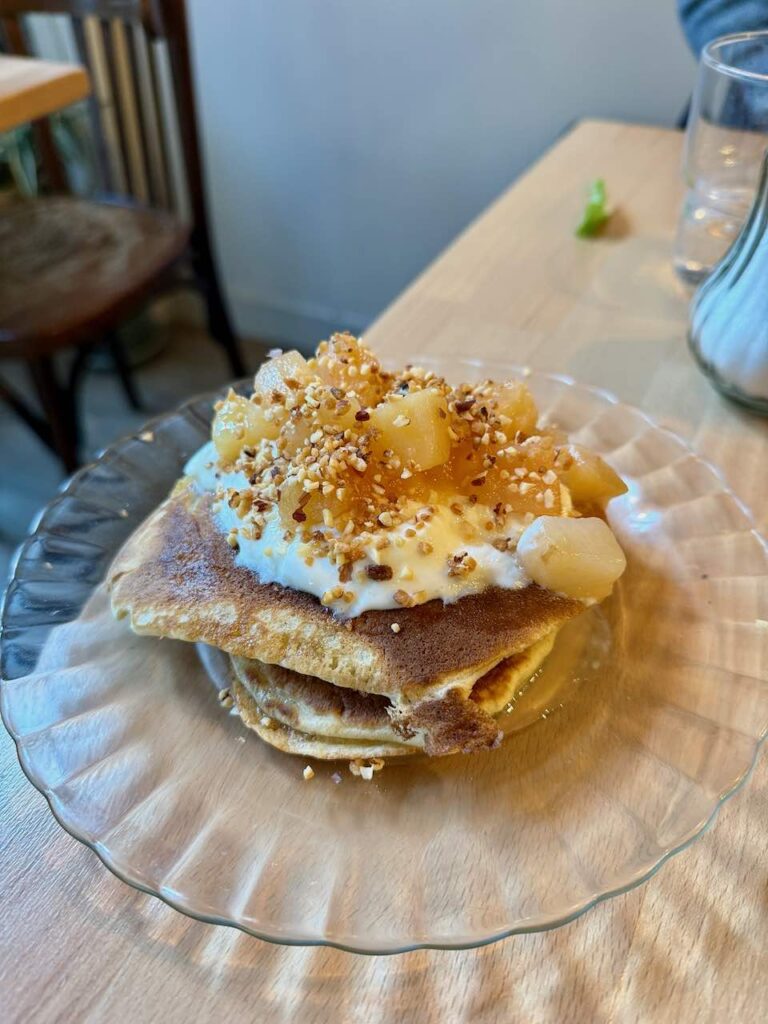 Pancakes surmontés de crème, de pommes cuites et de pralin dans une assiette en verre transparente
