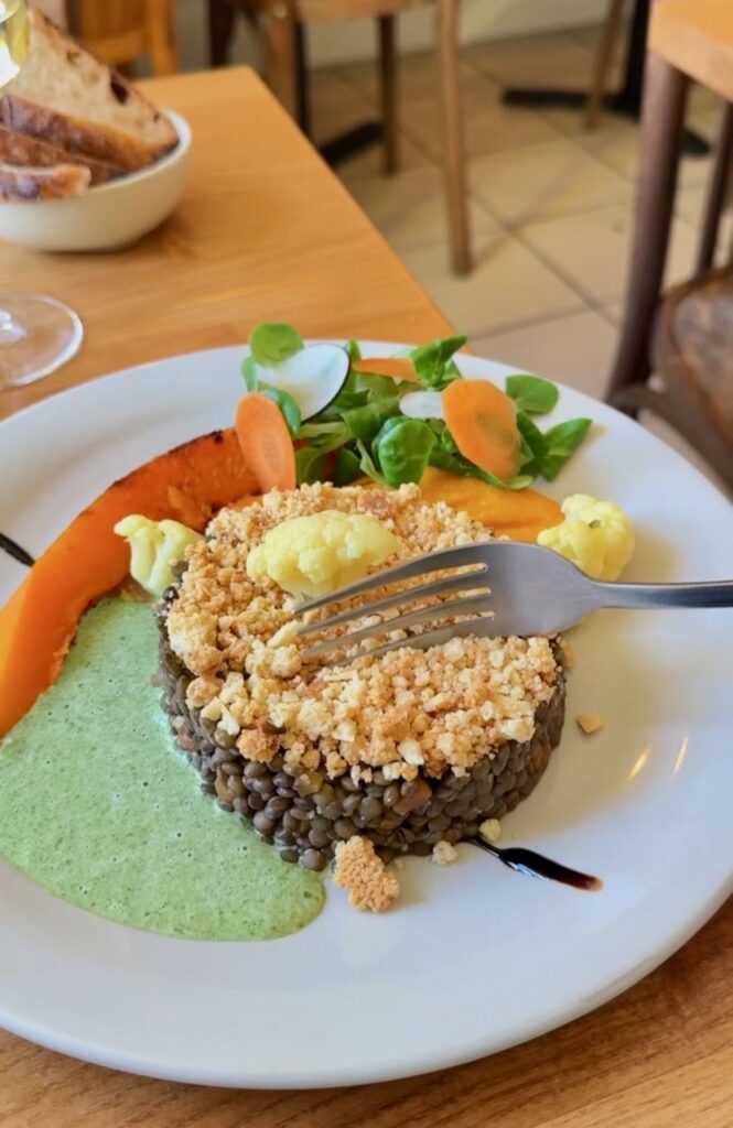 Crumble de lentilles, quartier de courge, mâche, pickles de carotte et chou fleur dans une assiette blanche et ronde