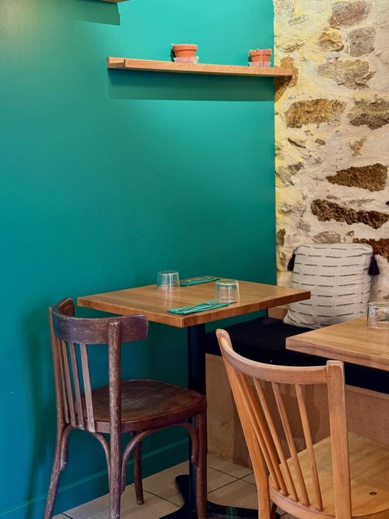 Vue sur une table et des chaises de bistro en bois, mur bleu canard et en pierres