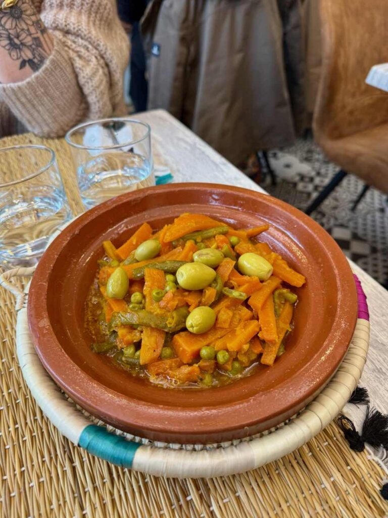 Carottes, olives vertes, haricots verts et petits-pois dans un plat à tajine en terre