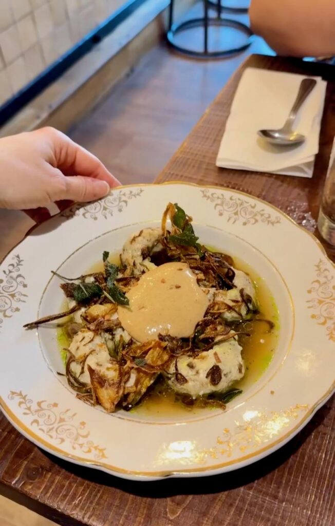 Ravioles accompagnées d'oignons frits dans un bouillon et servies dans une assiette creuse vintage blanche à liseré et ornements dorés