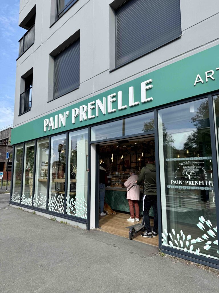 Devanture verte de la boulangerie avec plusieurs personnes faisant la queue