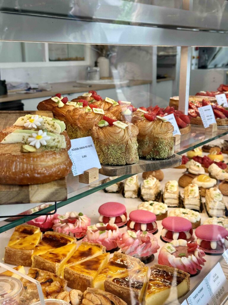 Viennoiseries et pâtisseries très colorées sur deux niveaux dans la vitrine, prix et noms affichés