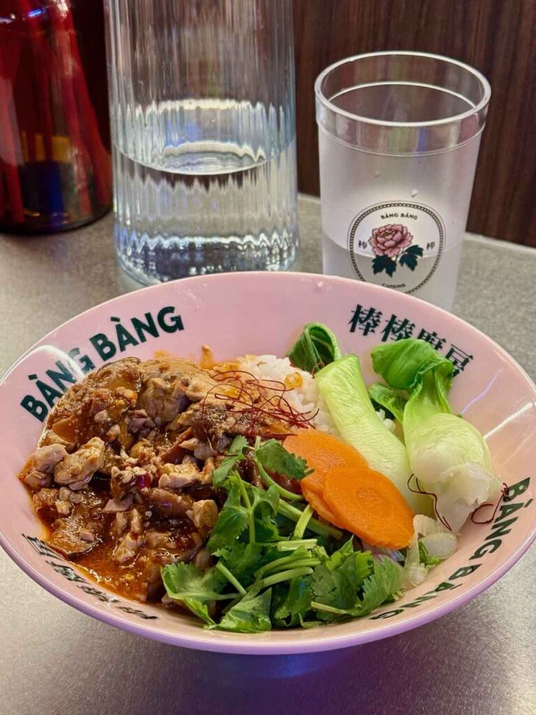 Tofu émietté, pak choi entier, coriandre, tranches de carottes, riz et sauce dans un bol rose pâle à l'effigie du restaurant