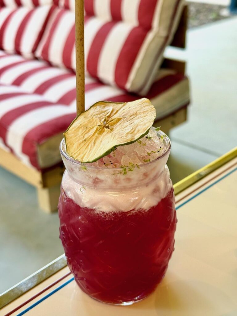 Mocktail rouge dans un verre en forme d'ananas, glace pilée sur le dessus et tranche de pomme séchée