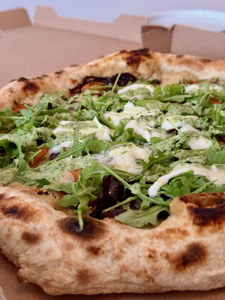 Vue rapprochée d'une pizza surmontée de roquette, mozza, carottes tranchées