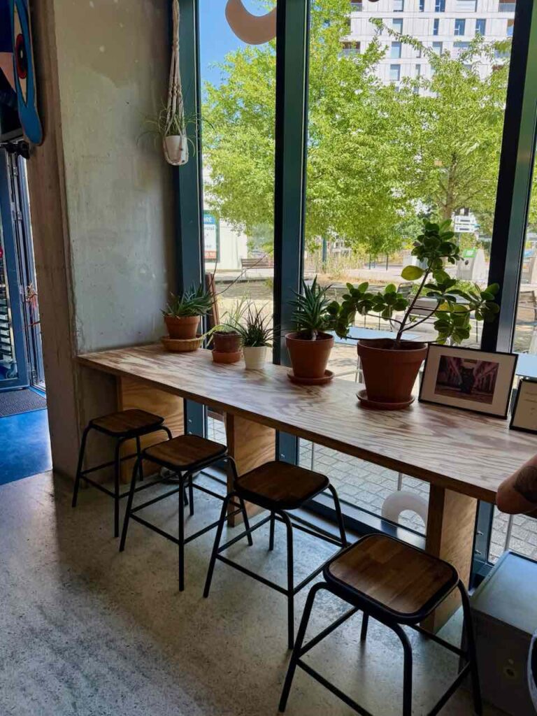 Comptoir en bois avec tabouret bois et métal sur lequel sont posées des plantes en pot, face vitrine