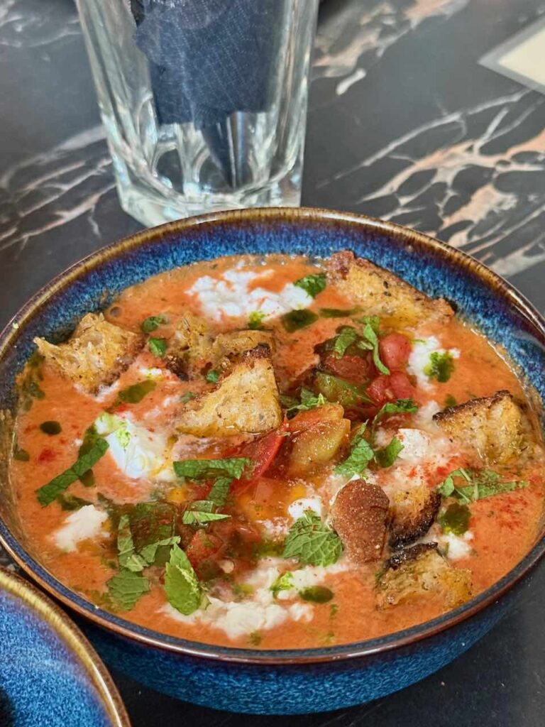 Gaspacho rouge avec croutons surmonté de menthe dans un bol bleu