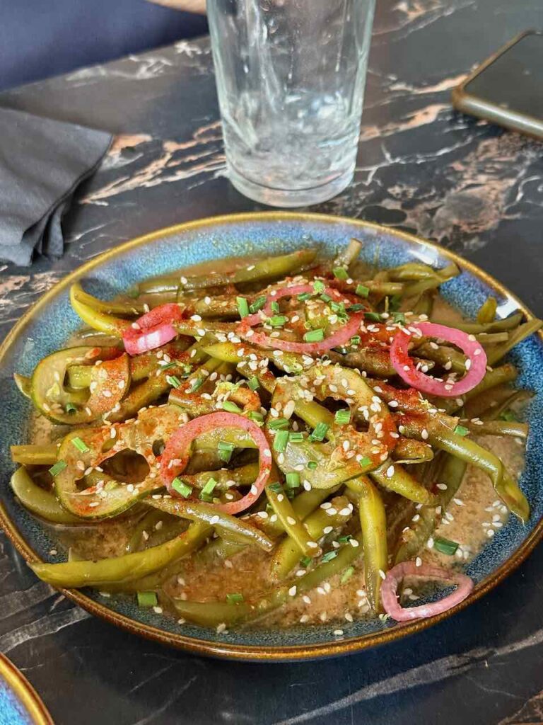 Haricots verts et pickles d'oignon rouge surmontés de graines de sésame dans une assiette bleue