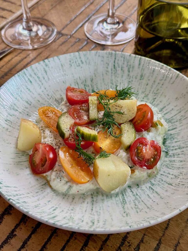 tsatziki, pommes de terre, tomates cerises, salicorne, concombre dans une assiette dans une assiette creuse blanche à liserés verts