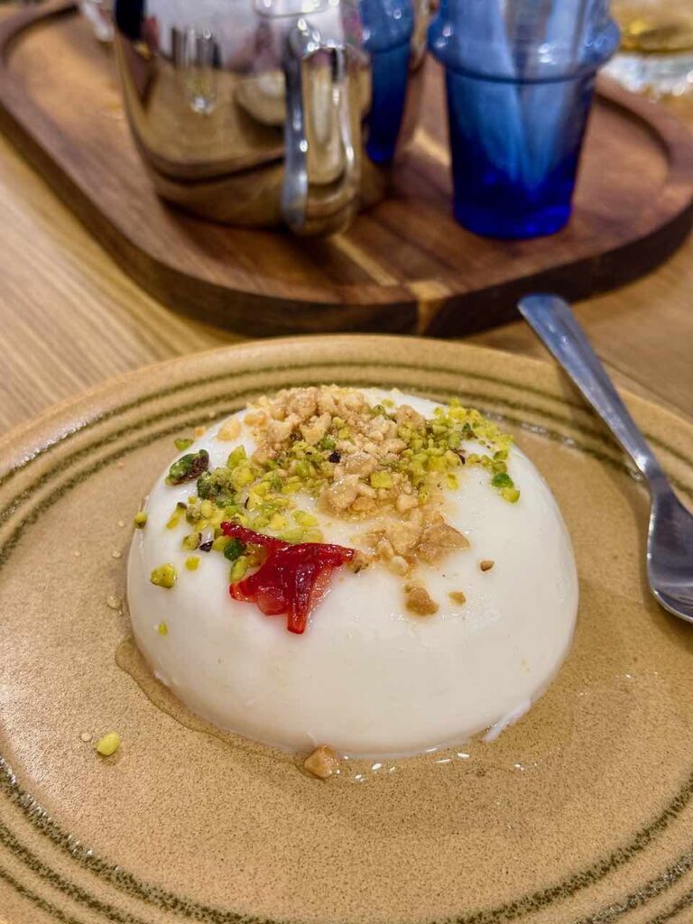 Flan rond, blanc et bombé surmonté de pistaches et cacahuètes dans une assiette ronde en grès