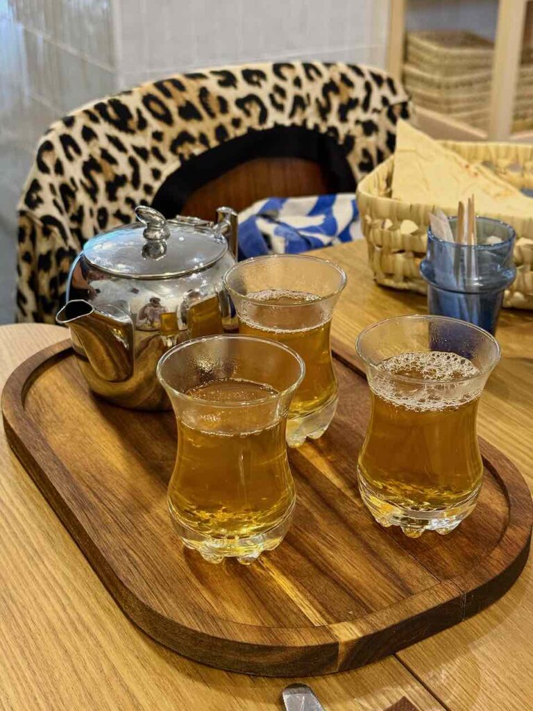 Trois petits verres remplis de thé, théière en métal à l'arrière plan, le tout posé sur un petit plateau en bois