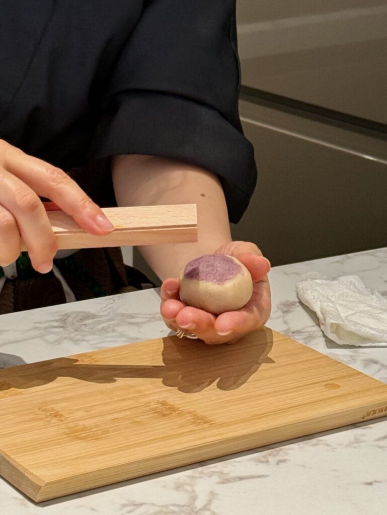 Personne en kimono noir tenant un wagashi dans une main, l'instrument en bois triangulaire dans l'autre