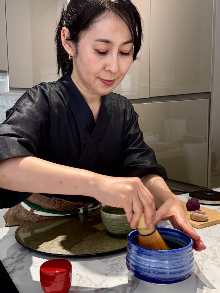 Personne portant un kimono noir et fouettant le matcha au chazen dans un bol bleu