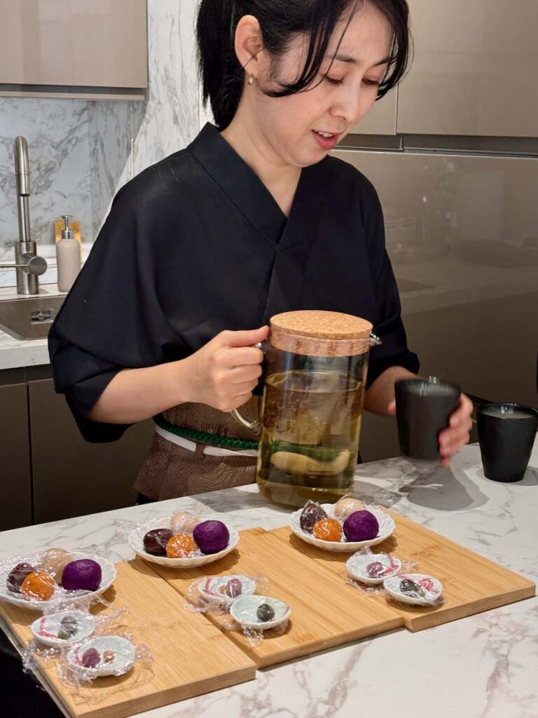 Personne en kimono noir servant un thé vert dans une tasse noir, préparations pour wagashi au premier plan